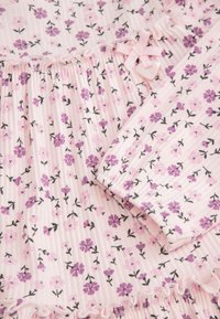 Materiał w kwiatowy wzór w odcieniach fioletu i różu na teksturowanym tle. Posiada falbaniasty brzeg oraz różową wstążkę z zawieszką w kształcie serca.