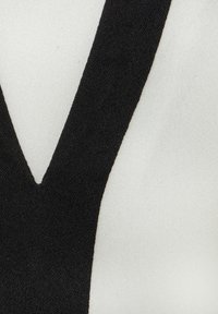 Zwarte stof met een V-vormige halslijn tegen een witte, gestructureerde achtergrond. Het materiaal lijkt zacht en enigszins doorzichtig.