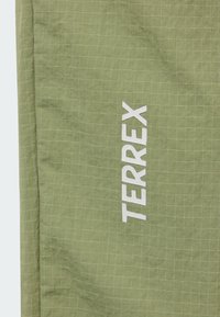 Gros plan sur un tissu ripstop vert clair avec un motif en quadrillage comprenant le logo blanc "TERREX" imprimé verticalement.