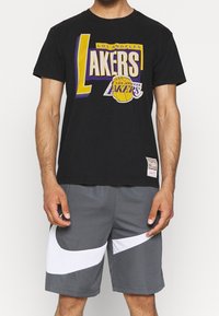 T-shirt in cotone nero con una grafica "Lakers" multicolore, abbinato a pantaloni sportivi grigi con strisce bianche a contrasto.