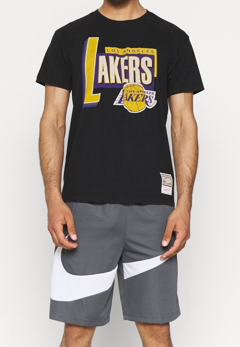 T-shirt in cotone nero con una grafica "Lakers" multicolore, abbinato a pantaloni sportivi grigi con strisce bianche a contrasto.