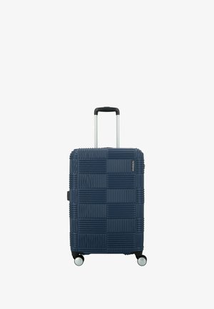 Maleta rígida de color azul oscuro, con textura estriada, asa retráctil y cuatro ruedas giratorias para facilitar la maniobrabilidad.