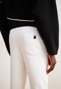 Hvide bomulds-sweatpants med en baglomme og et sort mærke. Den medfølgende sorte sweatshirt har en fuzzy tekstur og en cremefarvet accent.