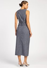 Grijze, mouwloze midi-jurk met een gladde textuur en subtiel ruitpatroon. Heeft een getailleerde corsage en een gestrikt accent in de taille.