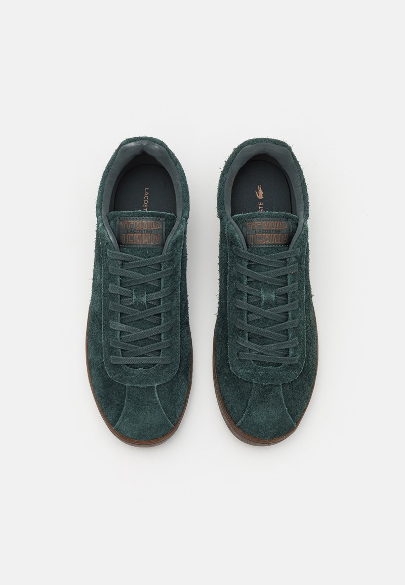 Zielone zamszowe sneakersy o niskim fasonie, z płaskimi sznurowadłami i teksturowaną powierzchnią; brązowa gumowa podeszwa z wytłoczonym logo na języku.