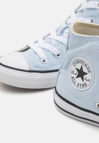 Modré plátnené vysoké tenisky s bielymi šnúrkami, gumovými špicami a čiernymi pruhmi. Obsahujú okrúhlu nálepku "Converse All Star".