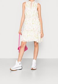 Floral-patterned white sleeveless dress with layered ruffles, paired with white high-top sneakers and a small pink handbag.