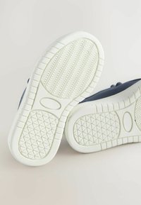 Marineblaue Sneakers mit strukturiertem Stoffobermaterial und weißen Gummisohlen. Die Sohlen weisen ein Zickzackmuster für Griffigkeit und Langlebigkeit auf.