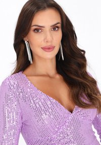 Rochie din sticlă lavandă cu un design înfășurat, având un decolteu adânc în V și mâneci lungi. Cercei cu franjuri argintii adaugă un detaliu de accent.