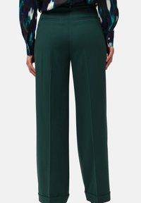 Pantaloni a gamba larga in tessuto verde scuro, con una texture liscia, due tasche posteriori e orlo rifinito.
