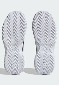 Scarpe da ginnastica nere con suole in gomma bianca caratterizzate da un motivo a spina di pesce. Include un logo sulla suola vicino al centro.