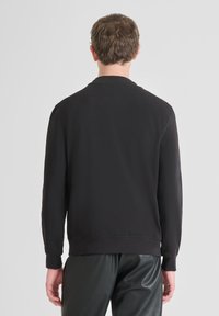 Zwart sweatshirt met een ronde hals en lange mouwen, met een gladde textuur en ribgebreide manchetten. Effen ontwerp aan de achterkant met subtiele branding boven de hals.