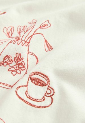 Izšūti audumi ar rozā dizainiem, kuros attēlots kafijas krūze un ziedu kanna uz krēmkrāsas fona, ar redzamu dūriena tekstūru.