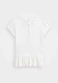 Biała koszula z krótkim rękawem, okrągłym dekoltem, zapinana na guziki z tyłu, z falbaniastym dołem. Wykonana z miękkiej bawełnianej tkaniny.