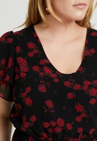 Svart blus med röda rosor, mjukt tyg, V-ringning, korta svängda ärmar och elastisk midja för avslappnad passform.