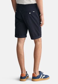 Shorts navy con dobladillos enrollados, hechos de una tela ligera. Presenta dos bolsillos traseros y una pequeña etiqueta de logo. Combinados con zapatillas azules.