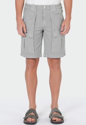 Man wearing light gray cargo shorts with multiple pockets, white top, and dark gray open-toe sandals standing against plain background.