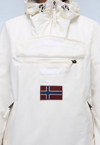 Weißer Anorak mit Kapuze, ausgestattet mit einer Fronttasche mit Reißverschluss, Klettverschluss-Akzenten und einem kastanienbraunen Patch mit einem blau-weißen Kreuzmuster.