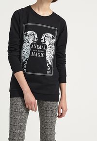 Sudadera negra con estampado gráfico de dos guepardos y el texto "ANIMAL OF THE WILD SIDE MAGIC" en blanco. Mangas largas, corte casual.