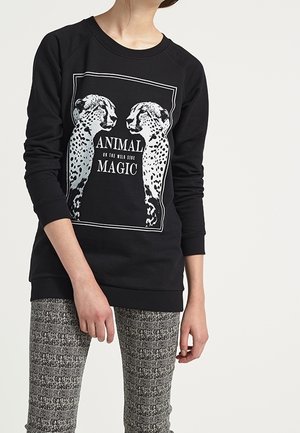 Sweatshirt noir avec un motif graphique de deux guépards et le texte "ANIMAL OF THE WILD SIDE MAGIC" en blanc. Manches longues, coupe décontractée.