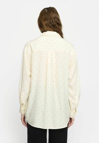 Helles gelbes Blusenshirt mit schwarzen Punkten, langen Ärmeln, Knopfmanschetten und einem lockeren Schnitt. Verfügt über eine Rückenpasse und einen weichen Stoff.