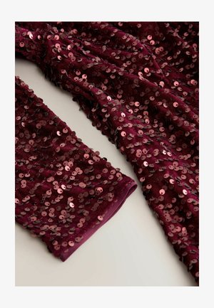 Burgundijska tkanina s sequinom z mehko teksturo, ki vsebuje tesno razporejene okrogle sequine. Rokavi so zapeti, kar dodaja podrobnosti oblikovanju.