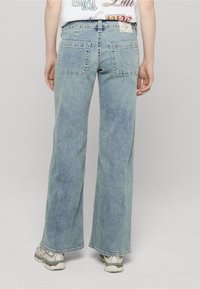 Světle modré džíny s širokými nohavicemi, prošitými zadními kapsami, vybledlou texturou a třepenými lemy. Nošeny se světlými teniskami.