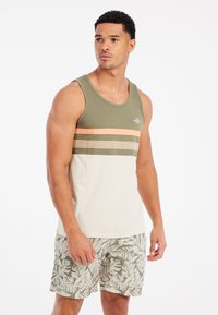 Canotta verde in cotone con righe orizzontali arancioni e beige, abbinata a pantaloni corti con motivo fogliare in tonalità di verde e beige.