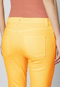 Gula denimjeans med en figurnära design, som har två bakfickor och synliga sömdetaljer. Slät struktur och ljus färg.