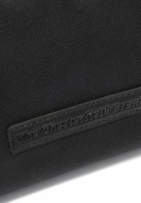 Pochette en tissu noir avec une surface texturée et une étiquette en cuir cousue embossée du nom "The Chesterfield Brand."