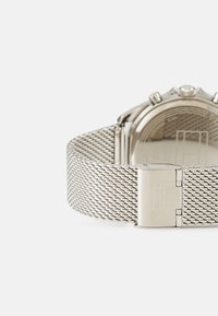 Silver metal mesh watch band with a clasp closure, featuring a smooth, polished watch face and subtle engraved details.