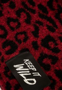 Tessuto in stampa leopardata rosso e nero con una texture pelosa; presenta un'etichetta nera con testo bianco che dice "KEEP IT WILD."