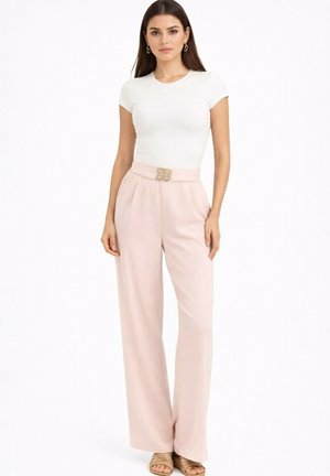 Femme portant un top blanc ajusté à manches courtes, un pantalon large taille haute rose clair avec une ceinture décorative à boucle, et des sandales.