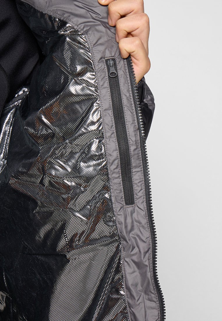 Interior de chaqueta aislante gris con un forro brillante y texturizado, y un bolsillo con cremallera. Una cremallera resistente recorre el borde.