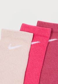 Tres pares de calcetines Nike de canalé en colores beige claro, rosa brillante y rosa intenso, con un pequeño logo blanco de Nike en cada uno.