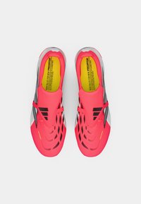 Φωτεινά ροζ αθλητικά παπούτσια με επάνω μέρος από δίχτυ, μαύρες λεπτομέρειες και υφή με σχέδιο. Διαθέτουν κίτρινη ετικέτα στη σόλα και κομψό, αεροδυναμικό σχεδιασμό.