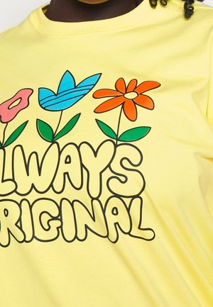 Žluté tričko s výrazným nápisem "Always Original" obklopené třemi stylizovanými květinami v růžové, modré a oranžové barvě s zelenými listy.