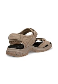 Beige sandaalit säädettävillä strapilla, pehmustettu musta pohja ja teksturoitu kumipohja, jossa on roiskeita. Kevyt ja ergonominen muotoilu.