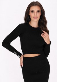 Top scurt negru cu nervuri și mâneci lungi, ce prezintă o decupare la talie și accente strălucitoare. Detalii cu nasturi pe mâneci.
