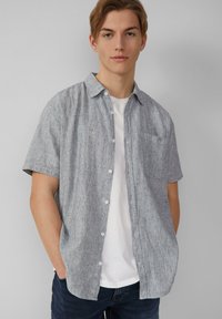 Korte mouwen, overhemd met kraag in grijs textiel met knoopsluiting. Inclusief een linker borstzak en gedragen over een wit t-shirt.