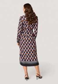Lange jurk met een geometrisch patroon in marineblauw, oranje en wit. Gedetailleerde manchetten en een contrasterende zwarte zoom, met een getailleerd ontwerp.