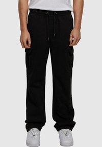Sorte cargo bukser med elastisk talje, sidelommer og afslappet pasform, parret med hvide sneakers på en neutral baggrund.