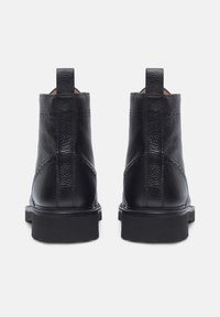 Stivali neri in pelle fino alla caviglia con superficie testurizzata, linguette posteriori e suole nere chunky, che mostrano un design elegante e privo di decorazioni.
