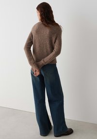 Bruin gebreid sweater met lange mouwen, losse pasvorm en ribboorden, gecombineerd met brede denim jeans, donkerblauw, met subtiele vervaging.