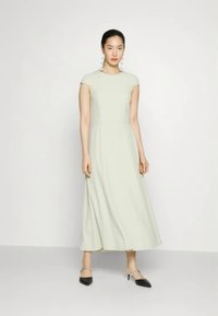 Light green, cap-sleeve maxi dress with a fitted bodice and flowing skirt. Worn with black pointed-toe heels and round earrings.