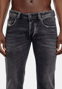 Dark gray denim jeans with a distressed finish, featuring front pockets and a button closure. Subtle wear patterns add texture.