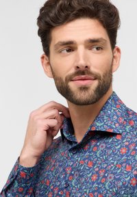 Kraagshirt met een blauwe achtergrond en multikleurige bloemmotieven. Het materiaal lijkt lichtgewicht met knoopaccenten op de mouwen.