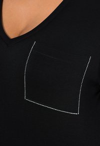 Schwarzes V-Neck-Shirt mit kurzen Ärmeln, ausgestattet mit einer rechteckigen Tasche, die mit Rhinestones verziert ist, und einem glatten Baumwollstoff.
