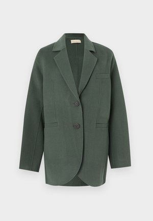 Veste en laine vert foncé à revers crantés, deux boutons, poches à rabat et manches longues, présentée sur fond blanc.
