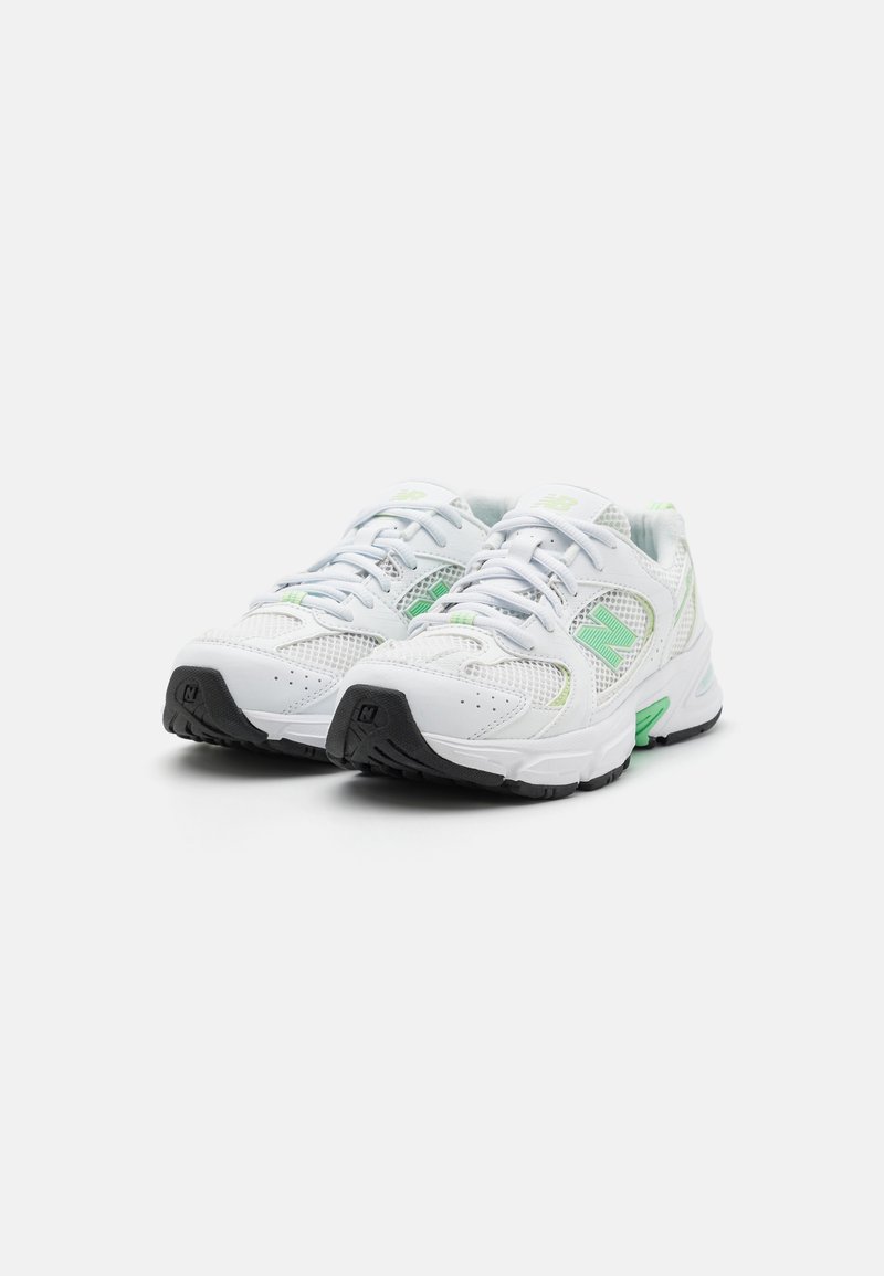 Zapatillas atléticas blancas hechas de material de malla y sintético. Presentan detalles en verde, suela de goma negra y un diseño tradicional con cordones.